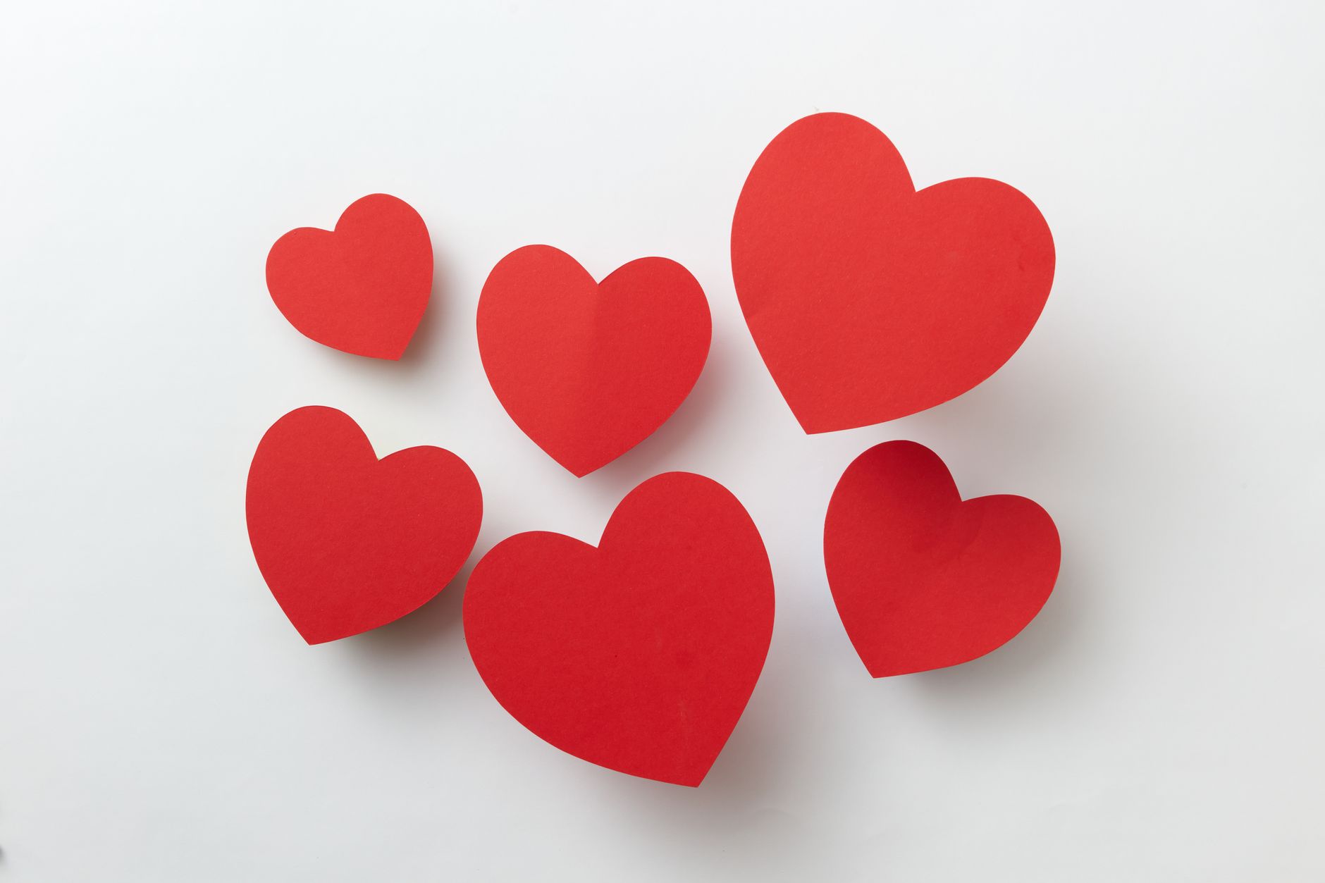 Flat lay of red paper hearts on a white surface, symbolizing love.
